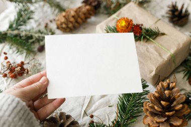 Noel kartı maketi. Köknar dalları ve çam kozalaklarıyla dolu boş bir tebrik kartı taşra masasında. Mesaj için yer var. İyi bayramlar. Sıfır atık posta kartı şablonu. Mutlu Noeller.