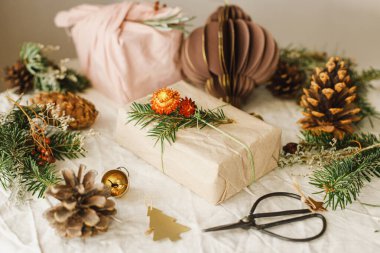 Sıfır boşa geçen Noel. Şık noel hediyeleri kumaş ve kağıda sarılmış, kır masasında köknar dalları ve doğal süsler. Kış çevre tatili, modern hediyeler. Mutlu Noeller.