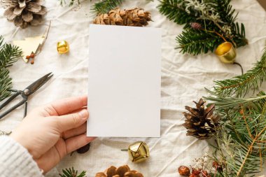 Noel kartı maketi. Köknar dalları ve çam kozalaklarıyla dolu boş bir tebrik kartı taşra masasında. Mesaj için yer var. İyi bayramlar. Sıfır atık posta kartı şablonu. Mutlu Noeller.