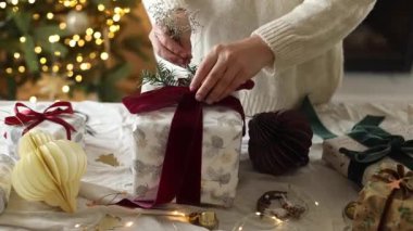 Eller modern Noel hediye kutusunu kırmızı kurdeleyle süslüyor ve masa üzerinde süslerle süslenmiş ışıklarla süsleniyor. Mutlu Noeller ve iyi tatiller.