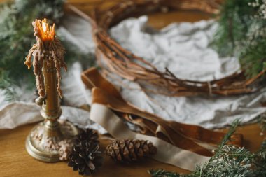 Noel kırsal çelengi yapıyorum. Evergreen dalları, kozalaklar, dallar, sicim, makas ve mum atmosferik festival odasındaki kırsal masada. Kış tatili hazırlıkları