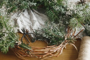 Şık, sade bir Noel çelengi yapıyorum. Çevreci dallar, dallar, sicim, makas atmosferik festival odasında kırsal masada. Kış tatili hazırlıkları, ayrıntılar