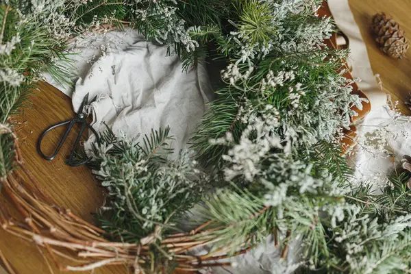 Şık, sade bir Noel çelengi yapıyorum. Evergreen dalları, çam kozalakları, dal, sicim, makas atmosferik festival odasında kırsal masada. Kış tatili hazırlıkları, ayrıntılar