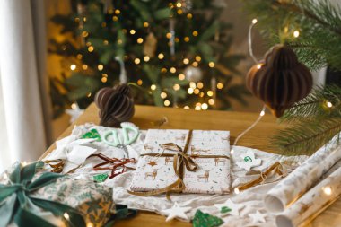 Mutlu Noeller! Şık bir Noel hediyesi, modern kağıt süsler ve altın noel ağacı ışıklarına karşı masa üzerinde çam dalları. Atmosferik Noel arifesi. Modern paketlenmiş hediye