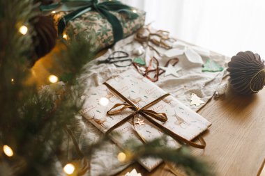 Şık bir Noel hediyesi, modern kağıt süslemeler ve arkaplandaki rustik masa üzerindeki çam dalları. Mutlu Noeller! Atmosferik Noel hazırlığı