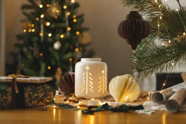 Şık bir Noel hediyesi, parlayan fener ve modern kağıt süslemeler arkadaki rustik masa üzerinde Noel ağacı ışıkları bokeh. Mutlu Noeller! Atmosferik Noel zamanı