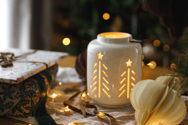 Şık bir Noel hediyesi, parlayan fener ve modern kağıt süslemeler arkadaki rustik masa üzerinde Noel ağacı ışıkları bokeh. Mutlu Noeller! Atmosferik Noel zamanı