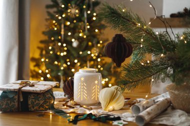 Şık bir Noel hediyesi, parlayan fener ve modern kağıt süslemeler arkadaki rustik masa üzerinde Noel ağacı ışıkları bokeh. Mutlu Noeller! Atmosferik Noel zamanı