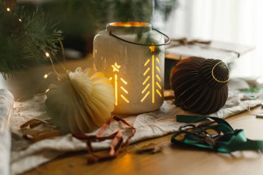 Şık noel feneri, hediye ve modern kağıt süslemeleri rustik masada altın noel ışıklarıyla. Mutlu Noeller! Atmosferik Noel zamanı, bayram afişi