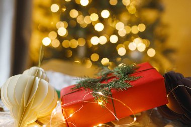 Modern dekorasyon ve kağıt süslemelerle süslenmiş şık bir Noel hediyesi. Arka planda Noel ağacı ışıkları var. Mutlu Noeller! Atmosferik Noel zamanı, bayram afişi