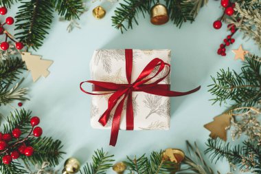 Şık bir Noel hediyesi. Kırmızı kurdele, yeşil köknar dalları, kırmızı böğürtlen ve mavi arka planda altın süslemelerle modern Noel hediyesi. Xmas geçmişi. Sezonun tebrik kartı.