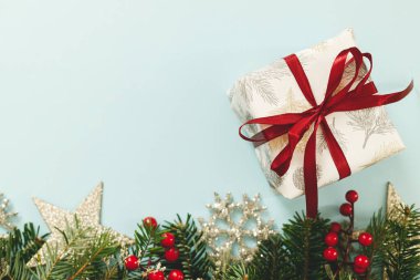 Kırmızı kurdeleli, yeşil köknar dallı, kırmızı böğürtlenli ve mavi arka planda parlak süslemeli şık bir Noel hediyesi. Mevsim selamları, mesaj için yer. Mutlu Noeller.!