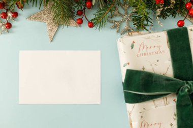 Noel kartı düz yatıyordu. Köknar dalları, kırmızı böğürtlen ve mavi arka planda hediye kutusu olan boş bir tebrik kartı. Mutlu noeller. Mevsimlik tebrik kartı şablonu