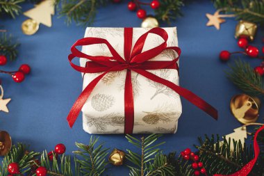 Mutlu Noeller! Kırmızı kurdele, yeşil köknar dalları, kırmızı böğürtlen ve mavi arka planda altın süslemeleri olan şık bir Noel hediyesi. Xmas geçmişi. Mutlu Noeller.
