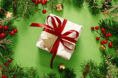 Şık bir Noel hediyesi. Kırmızı kurdele, yeşil köknar dalları, kırmızı böğürtlen ve yeşil arka planda altın süslemelerle modern Noel hediyesi. Xmas geçmişi. Sezonun tebrik kartı.