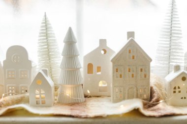 Noel seramik evleri, karlı ağaçlar ve penceredeki rahat eşarbın üzerindeki ışıklar. Xmas geçmişi. Mutlu Noeller! Noel sahnesi, minyatür tatil köyü. Tatil modern dekorasyonlar