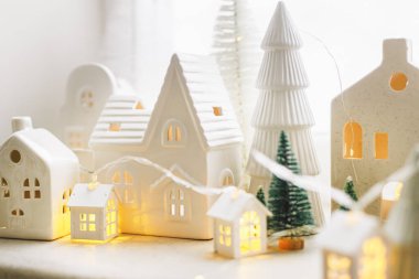 Noel seramik evleri, beyaz karlı ağaçlar ve penceredeki altın ışıklar. Xmas geçmişi. Mutlu Noeller! Atmosferik Noel sahnesi, minyatür tatil köyü