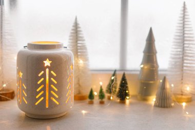 Merry Christmas! Stylish glowing christmas lantern and winter tree decorations on window with golden lights bokeh. Atmospheric magical scene. Christmas holiday banner. Space for text clipart