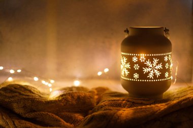 Mutlu Noeller! Şık, ışıl ışıl bir Noel feneri ve akşam karlı bir pencerede rahat bir süveterin üzerinde altın ışıklar. Atmosferik büyülü sahne. Noel tatili afişi. Metin için boşluk