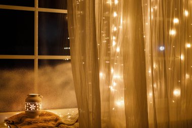 Işıldayan noel feneri, altın ışıklarla donuk pencere pervazında örülmüş süveter. Atmosferik büyülü natürmort. Mutlu Noeller ve mutlu tatiller! Kış duvar kağıdı