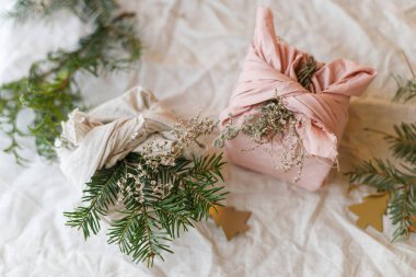 Sıfır atık Noel yatıyordu. Renkli Noel hediyeleri, keten kumaşa sarılı, yeşil köknar dalı, kır masasında, doğal süslemelerle. Sürdürülebilir yaşam tarzı, Furoshiki sunar