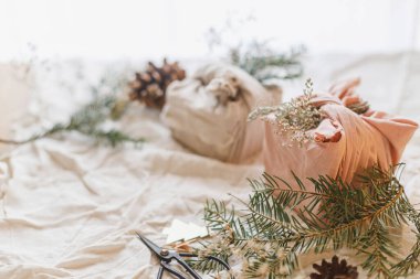 Sıfır Noel konsepti. Renkli Noel hediyeleri, keten kumaşa sarılı, yeşil köknar dalı, kır masasında, doğal süslemelerle. Sürdürülebilir yaşam tarzı, Furoshiki sunar