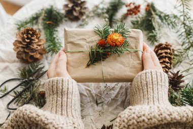 Sıfır atık Noel yatıyordu. Kırsal masada doğal süslemelerle süslenmiş köknar dalıyla süslü Noel hediyeleri tutan eller. Sürdürülebilir hediyeler, kış tatili hediyesi