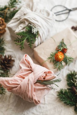 Köy masasında, çam kozalakları ve kurumuş böğürtlenli sıfır atık hediyesi. Mutlu Noeller! Modern basit paketlenmiş hediye kutuları ve doğal süsler. Sürdürülebilir yaşam tarzı