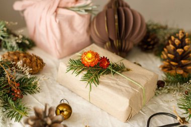 Köy masasında, çam kozalakları ve kurumuş böğürtlenli sıfır atık hediyesi. Mutlu Noeller! Modern basit paketlenmiş hediye kutuları ve doğal süsler. Sürdürülebilir yaşam tarzı