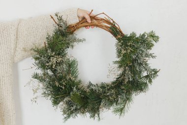 Beyaz arka planda şık bir Noel çelengi tutan kazaklı kadın. Kış tatili hazırlığı. Mutlu Noeller.