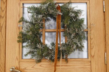 Ön kapısında kurdele asılı, şık bir Noel rustik çelengi. Kapatın. Modern ev girişi ya da kış tatili için veranda dekorasyonu. Mutlu Noeller ve mutlu tatiller