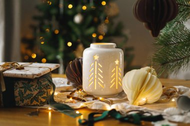 Mutlu Noeller ve mutlu Noeller! Şık bir Noel hediyesi, parlayan bir fener, altın Noel ağacı ışıklarına karşı masanın üstünde modern kağıt süsler. Atmosferik Noel arifesi, büyülü tatil zamanı.