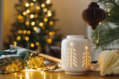 Mutlu Noeller ve mutlu Noeller! Şık bir Noel hediyesi, parlayan bir fener, altın Noel ağacı ışıklarına karşı masanın üstünde modern kağıt süsler. Atmosferik Noel arifesi, büyülü tatil zamanı.