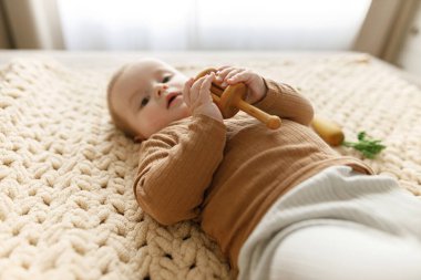 Tahta oyuncaklar tutan ve yatağa uzanan sevimli bebek. Çocukluk. Eko oyuncaklarla oynayan sevimli bebek portresi
