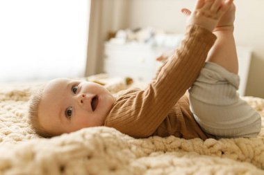 Ayakları yatakta oynayan sevimli, mutlu bir bebek. Çocukluk mutluluğu. Gülümseyen ve rahatlatan sevimli çocuk portresi