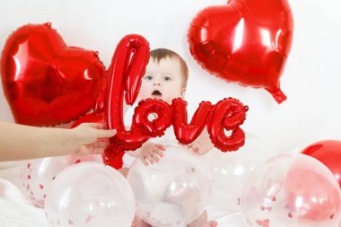 Bebek Valentine. İçeride kırmızı kalp şeklinde balonlarla oynayan sevimli bir çocuk. Sevgililer günün kutlu olsun. Sevgililer günü dekorunun arasında gülümseyen sevimli bir bebek.