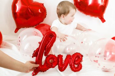 Bebek Valentine. İçeride kırmızı kalp şeklinde balonlarla oynayan sevimli bir çocuk. Sevgililer günün kutlu olsun. Sevgililer günü dekorunun arasında gülümseyen sevimli bir bebek.