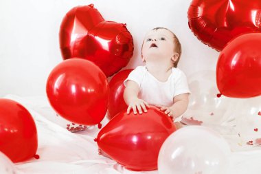 Bebek Valentine. İçeride kırmızı kalp şeklinde balonlarla oynayan sevimli bir çocuk. Sevgililer günün kutlu olsun. Sevgililer günü dekorunun arasında gülümseyen sevimli bir bebek.