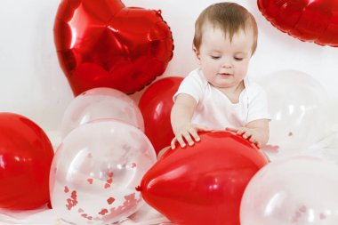 Bebek Valentine. İçeride kırmızı kalp şeklinde balonlarla oynayan sevimli bir çocuk. Sevgililer günün kutlu olsun. Sevgililer günü dekorunun arasında gülümseyen sevimli bir bebek.