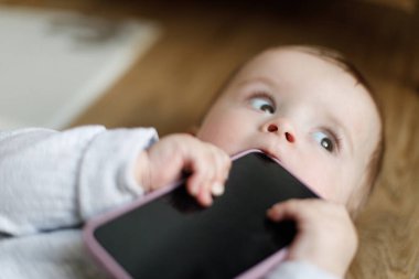 Sevimli bebek kucağında ve akıllı telefon çiğniyor. Bebek gelişimi için aktivite zamanı ve ekran zamanı. Bebek elleriyle telefonu kapat.