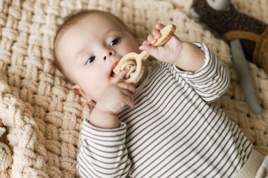 Örgü örülmüş battaniyenin üzerinde ahşap bir iple uzanmış şirin bir bebek. Ahşap oyuncaklar taşıyan sevimli bebek portresi, yazı için yer. Çocukluk ve çocuk bakımı