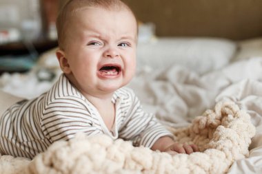 Sabahın köründe örgü örmüş battaniyeye uzanmış ağlayan şirin bir bebek. Yatma vakti. Üzücü duyguları olan bebek portresi, yazı için yer. Çocukluk ve çocuk bakımı
