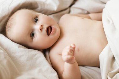 Sabah güneşinde bej çarşaflarda yatan şirin küçük bebek. Uyku ya da uyanma zamanı. Yatakta bebek portresi, mesaj için yer. Çocuk uykusu ve çocuk bakımı