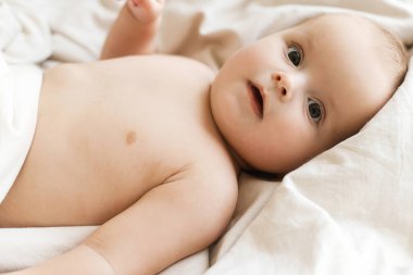 Sabah güneşinde bej çarşaflarda yatan şirin küçük bebek. Uyku ya da uyanma zamanı. Yatakta bebek portresi, mesaj için yer. Çocuk uykusu ve çocuk bakımı