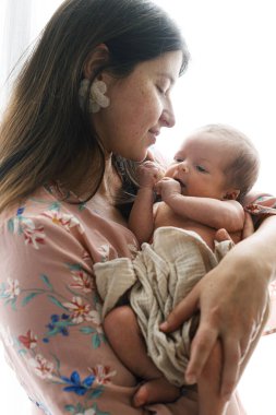 Mutlu Anne pencerenin ışığında küçük şirin bir bebek tutuyor. Yaklaş. Anneler Günün kutlu olsun! Annelik ve ebeveynlik. Evlat edinme ve doğurganlık kavramı