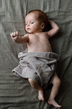 Kahverengi yatağa uzanmış, güzel, küçük bir oğlan çocuğu. Annelik ve ebeveynlik. Şık keten tekstil içinde şirin bir bebek. Evlat edinme ve doğurganlık kavramı