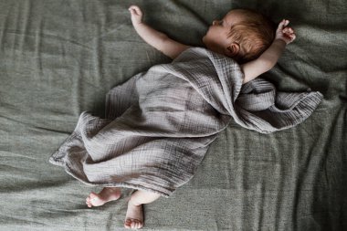 Kahverengi yatağa uzanmış, güzel, küçük bir oğlan çocuğu. Annelik ve ebeveynlik. Şık keten tekstil içinde şirin bir bebek. Evlat edinme ve doğurganlık kavramı