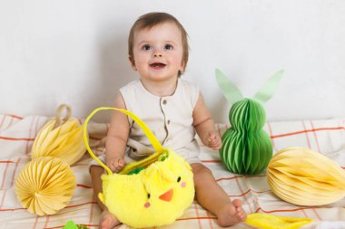 Mutlu Paskalyalar! Renkli paskalya kağıtlı yumurtaları, sepeti, şenlikli dekorasyonu ve havuçları olan şirin bir bebek. Sevimli Paskalya tavşanı ve Paskalya avı.