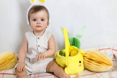 Renkli yumurtalar ve sepetten çıkan havuçlarla oynayan tavşan kulaklı şık bir Paskalya bebeği. Sevimli Paskalya tavşanı ve Paskalya avı konsepti. Mutlu Paskalyalar