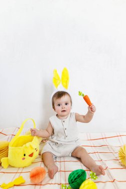 Mutlu Paskalyalar! Renkli paskalya kâğıdı yumurtaları, şenlikli dekorasyon ve havuçlarla oturan tavşan kulaklı şirin bir bebek. Sevimli Paskalya tavşanı ve Paskalya avı.